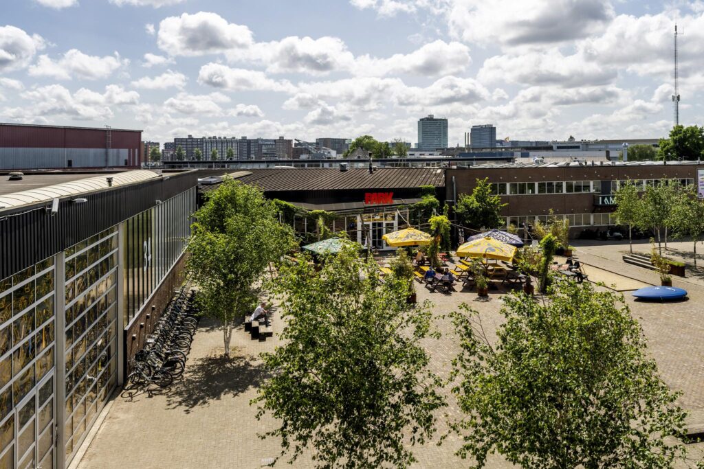 Courtyard with outdoor seating and colorful umbrellas in front of the PARK building on Johan van Hasseltweg.